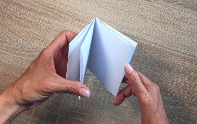 Händer viker ett vitt papper till ett litet zine vid ett träbord