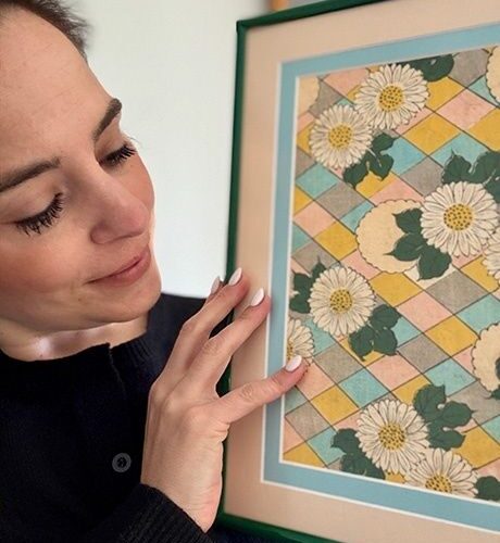Person håller upp en grönramad tavla med blommigt motiv