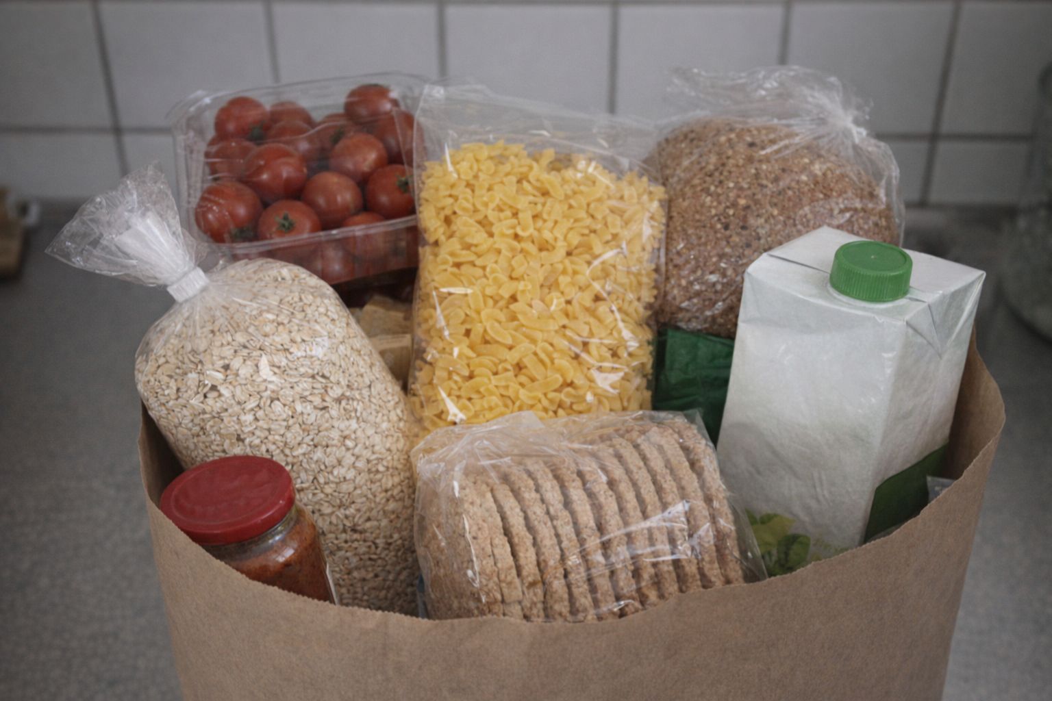 Matvaror i en papperskasse: havregryn, pasta, tomater, knäckebröd, mjölkförpackning.